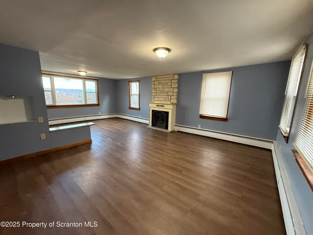an empty room with wooden floor fireplace and windows
