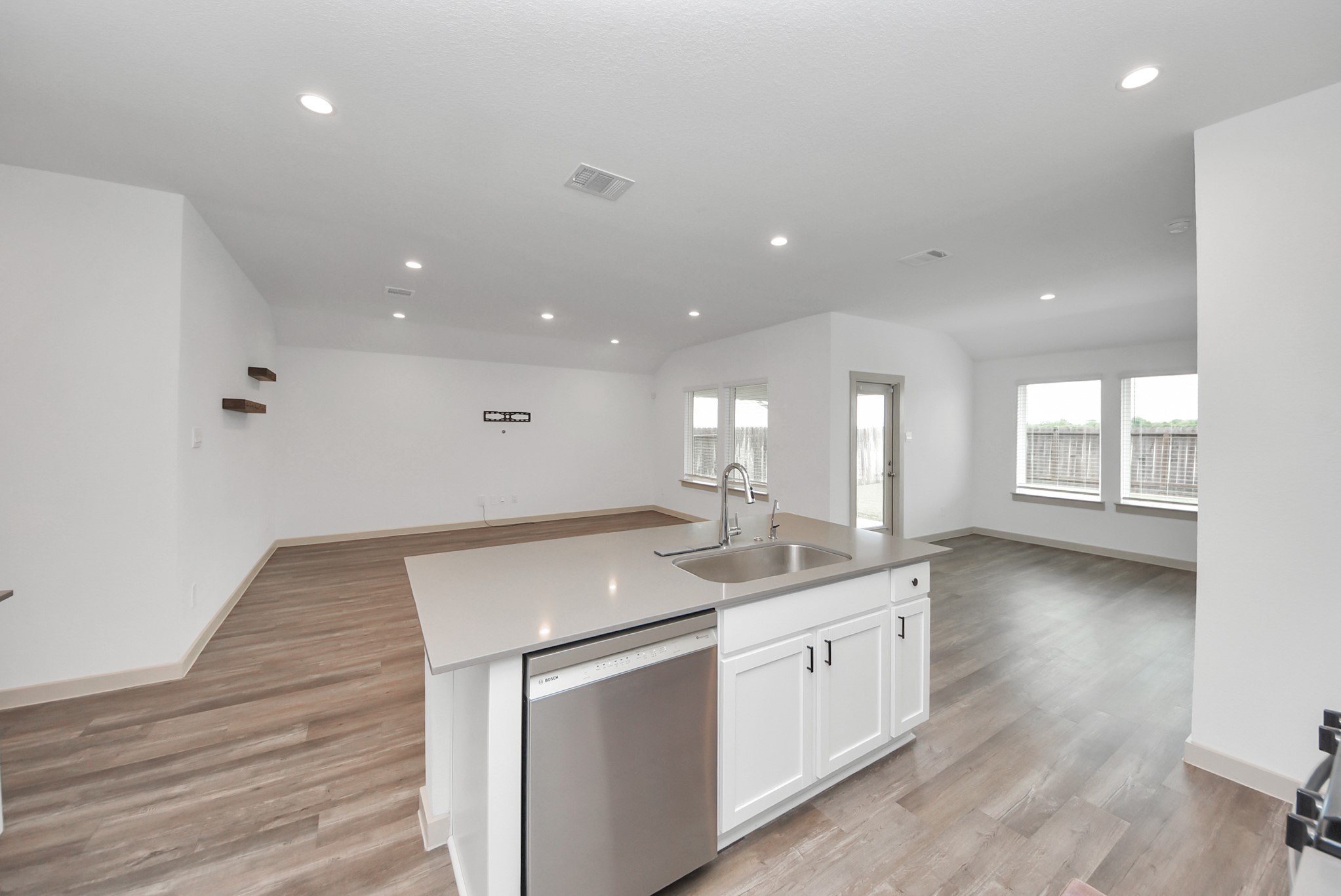 7911 Wrangler Shack Lane Rosharon, TX 77583 - Photo 3 of 40 Spacious open-concept living area with modern kitchen featuring a sleek island, ample natural light from large windows, and stylish wood flooring.
