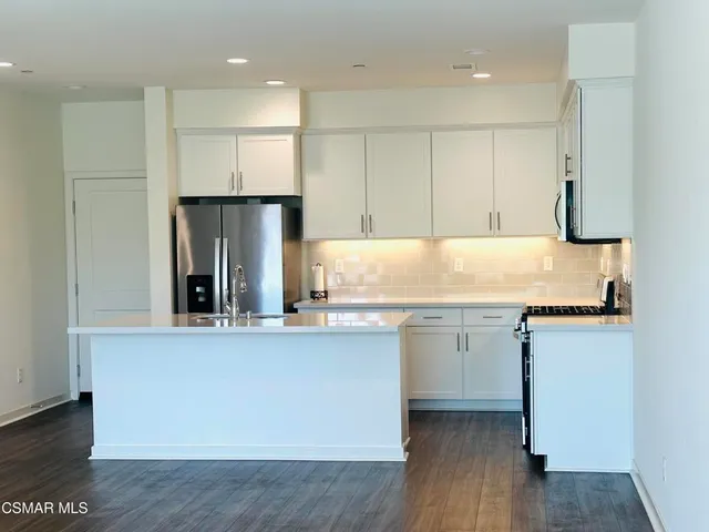 a kitchen with kitchen island a sink a stove a refrigerator and white cabinets