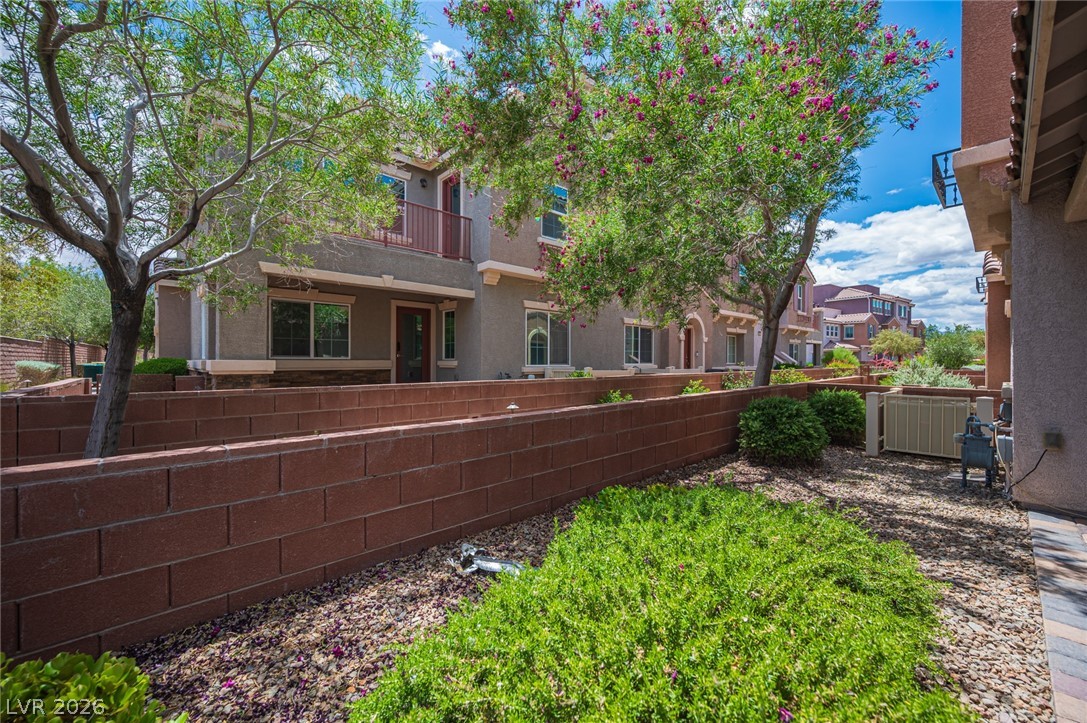 9916 Sable Point Street Las Vegas, NV 89178 - Photo 3 of 73 A tiered landscape with lush greenery complements the charming two-story residential structures under a bright sky.