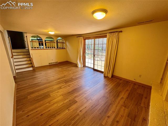 280 Raven Hills Road Colorado Springs, CO 80919 - Photo 38 of 48 Unfurnished room featuring visible vents, wood finished floors, baseboards, stairway, and a textured ceiling
