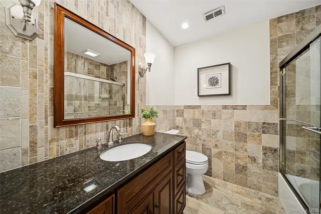 a bathroom with a granite countertop sink a mirror a toilet and a shower