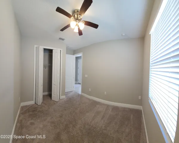 an empty room with chandelier fan and windows