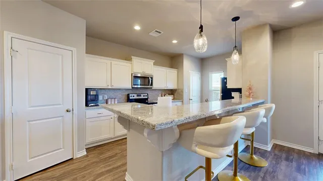 a kitchen with stainless steel appliances granite countertop a sink a stove a refrigerator and island with wooden floor