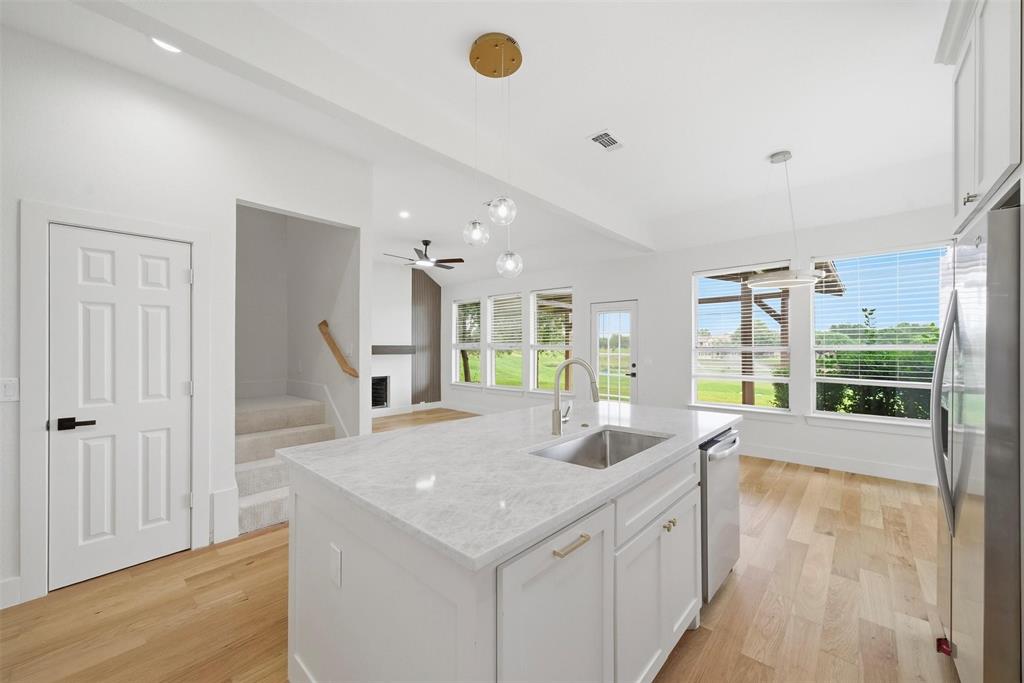 2104 Old McGarrah Road McKinney, TX 75072 - Photo 1 of 35 Kitchen island with a built-in sink, stainless steel appliances, wood-finish flooring, and multiple windows