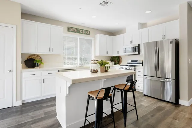 a kitchen with stainless steel appliances a refrigerator a stove a sink and white cabinets with wooden floor