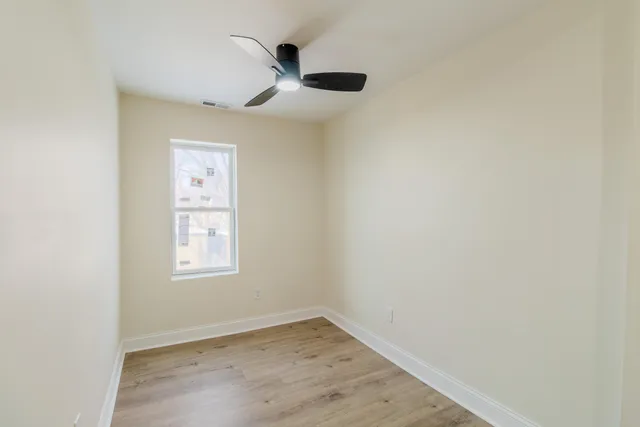 an empty room with wooden floor chandelier fan and windows