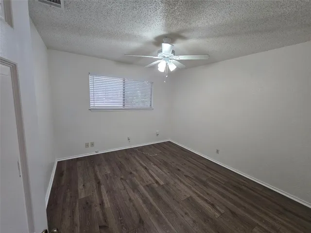 an empty room with a chandelier fan and wooden floor