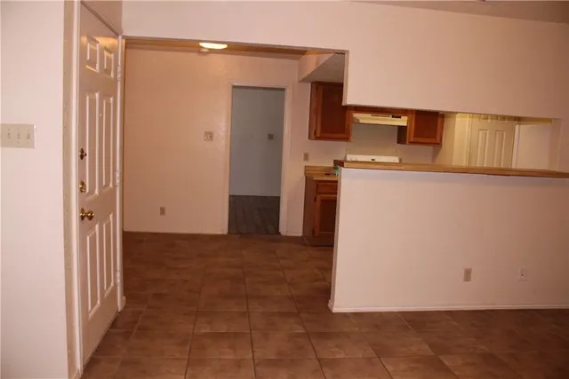 a view of a refrigerator in kitchen and an empty room with wooden floor