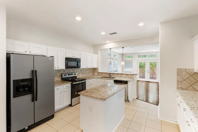 a kitchen with stainless steel appliances granite countertop a refrigerator oven a sink dishwasher and white cabinets with wooden floor