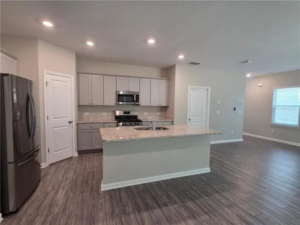 a kitchen with stainless steel appliances granite countertop a refrigerator a stove top oven a sink and white cabinets with wooden floor