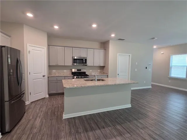 a kitchen with stainless steel appliances granite countertop a refrigerator a stove top oven a sink and white cabinets with wooden floor