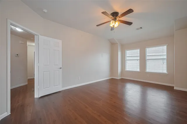 a view of an empty room with wooden floor and a ceiling fan
