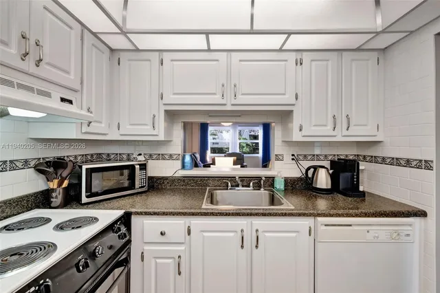 a kitchen with granite countertop a stove a sink and a white cabinets