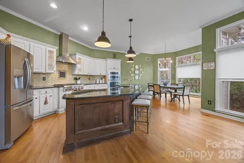 a kitchen with stainless steel appliances granite countertop a stove a refrigerator a oven a sink a dining table and chairs with wooden floor