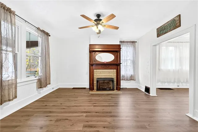 an empty room with wooden floor a ceiling fan a fireplace and windows