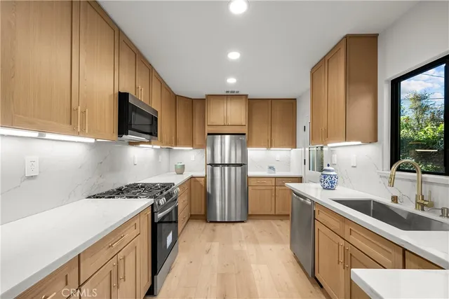 a kitchen with stainless steel appliances granite countertop a refrigerator a stove and a sink with wooden floor