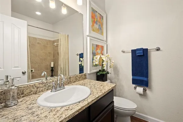a bathroom with a granite countertop sink a toilet a mirror and shower