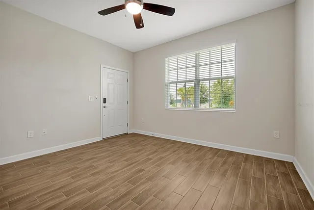 an empty room with wooden floor chandelier fan and windows