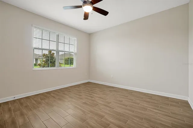 an empty room with wooden floor chandelier fan and windows