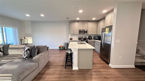 a living room with stainless steel appliances furniture wooden floor and a window