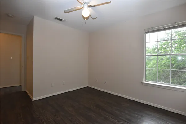 an empty room with wooden floor fan and windows