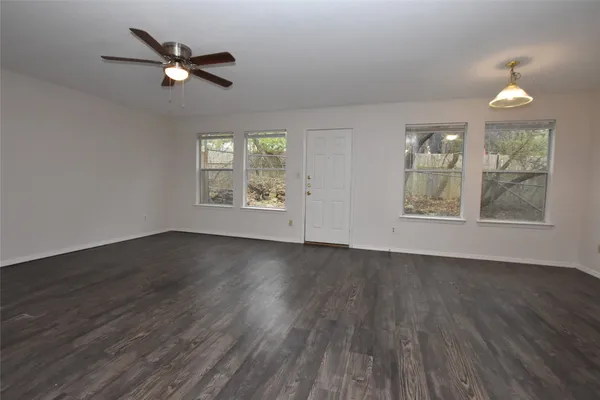 an empty room with wooden floor chandelier fan and windows