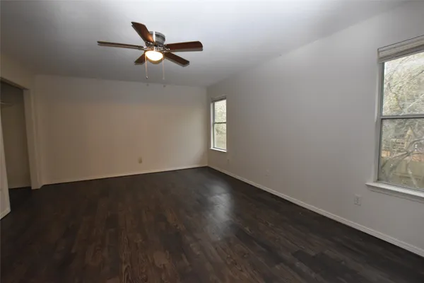 an empty room with wooden floor fan and windows