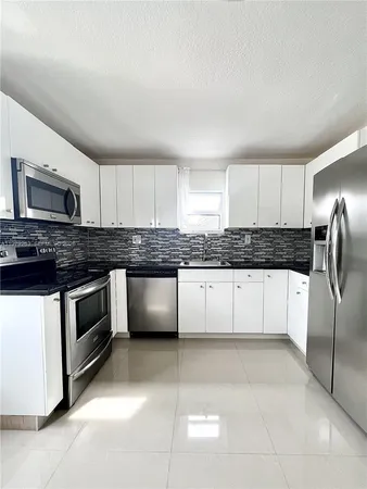 a kitchen with granite countertop a refrigerator and white cabinets
