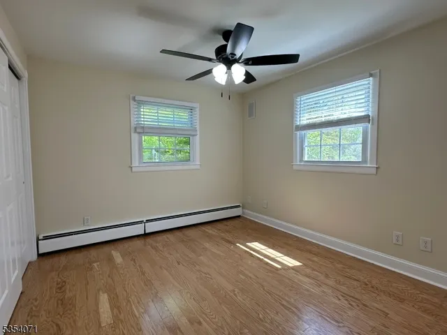 an empty room with wooden floor chandelier fan and windows