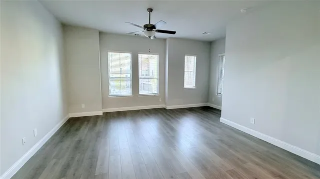 an empty room with wooden floor chandelier fan and windows