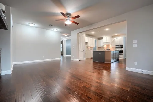 an empty room with wooden floor kitchen view and a chandelier