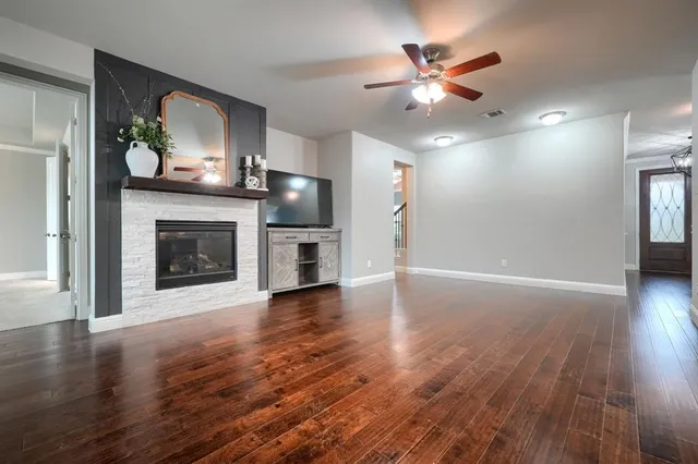an empty room with fireplace wooden floor chandelier fan and windows