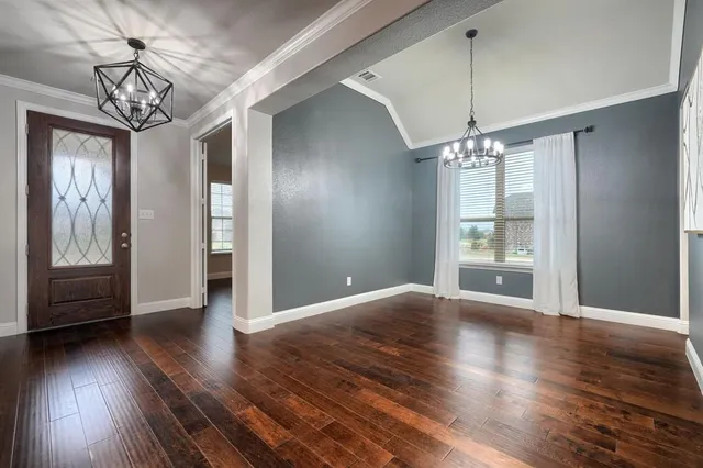 a view of an empty room with wooden floor and a chandelier