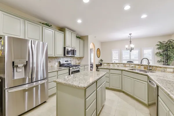 a kitchen with stainless steel appliances granite countertop a refrigerator a sink dishwasher a stove and white countertops with wooden floor
