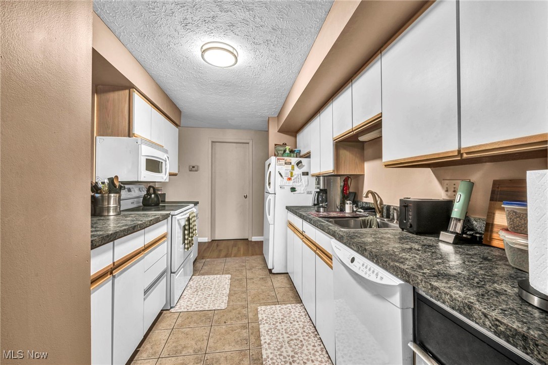4750 Oak Point Road, Unit 304 Lorain, OH 44053 - Photo 11 of 29 Kitchen featuring white appliances, white cabinets, a textured ceiling, dark countertops, and light tile patterned floors