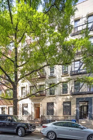 a front view of a building with lot of cars and trees