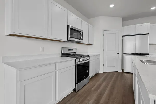 a kitchen with stainless steel appliances a stove top oven a sink a refrigerator white cabinets and wooden floor