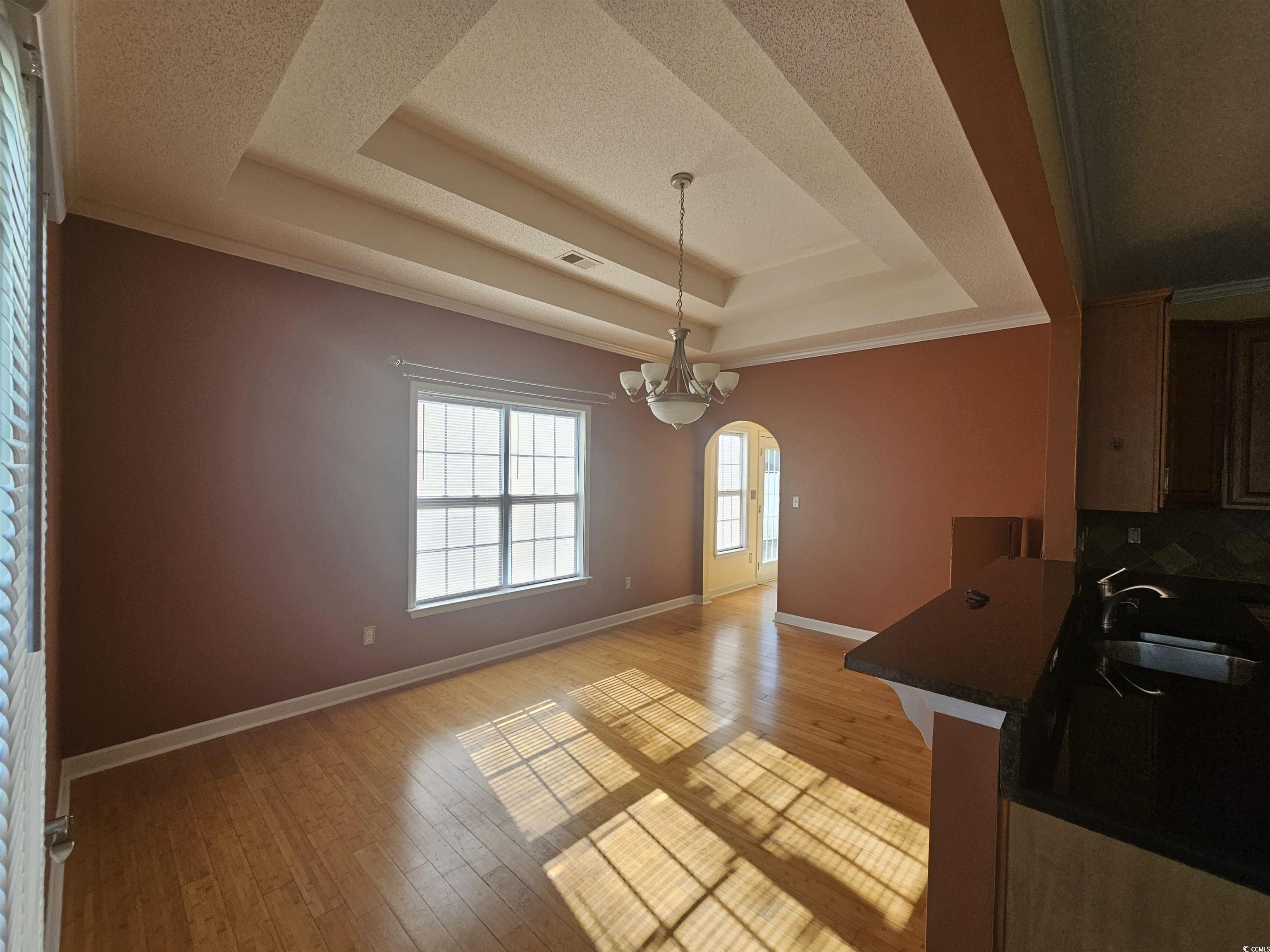 1011 Hillsdale Little River, SC 29566 - Photo 9 of 21 Unfurnished dining area with a raised ceiling, arched walkways, light wood-type flooring, ornamental molding, and a textured ceiling