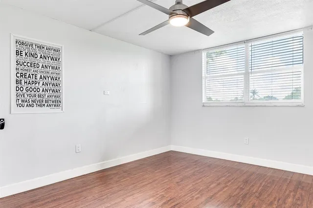 an empty room with wooden floor fan and windows