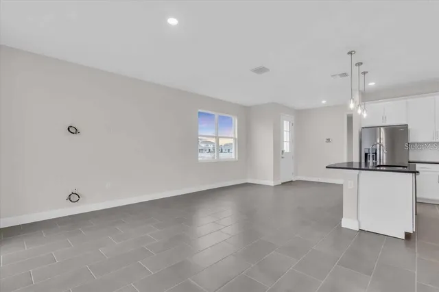 a view of an empty room with window and a kitchen view