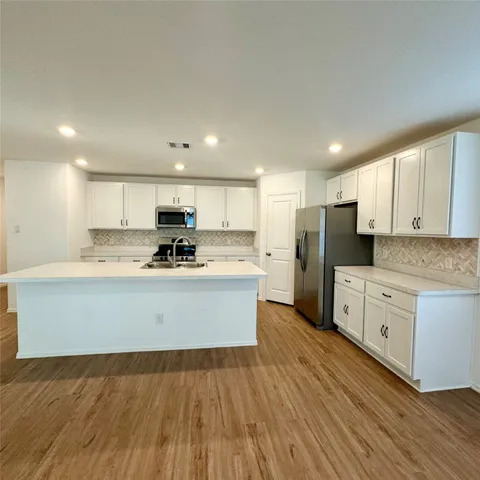 a large white kitchen with kitchen island a sink wooden floor white stainless steel appliances and cabinets