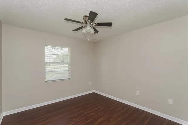 an empty room with wooden floor fan and windows