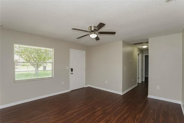 a view of an empty room with wooden floor and a ceiling fan