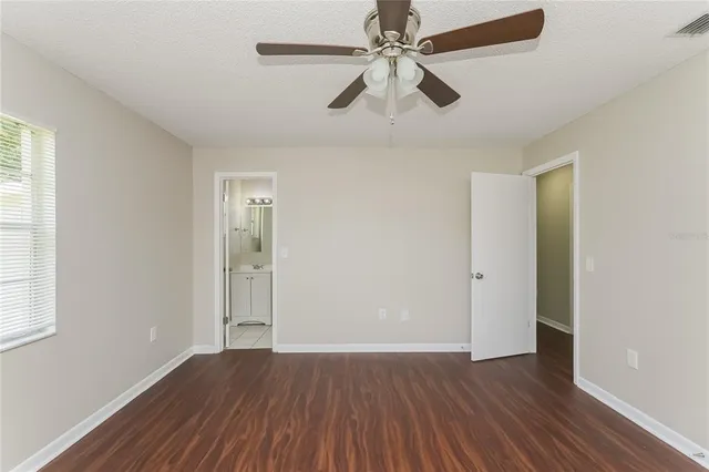 an empty room with wooden floor fan and windows