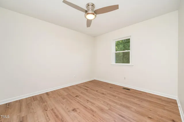 an empty room with wooden floor and a ceiling fan