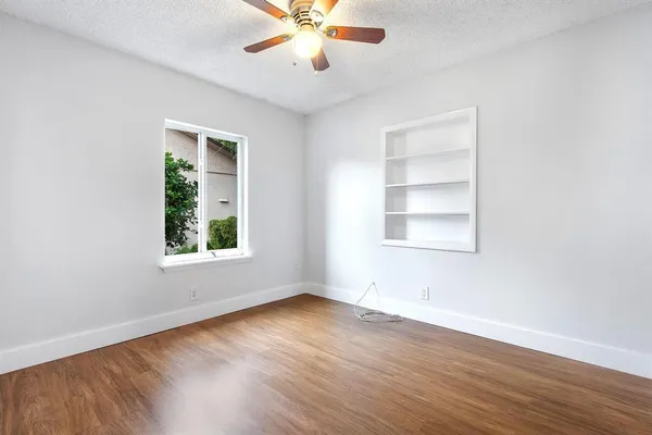 an empty room with wooden floor chandelier fan and windows