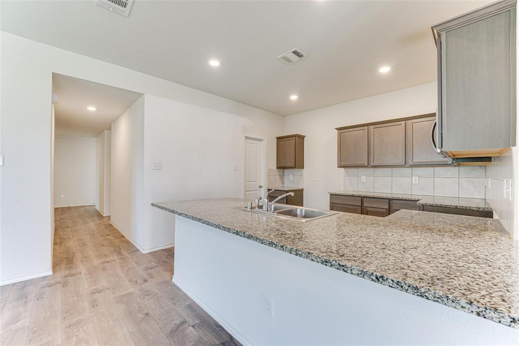 517 Milo Way Royse City, TX 75189 - Photo 4 of 34 Kitchen featuring an expansive granite countertop island with an undermount double-basin sink, light wood-finish flooring, recessed lighting, and grey cabinetry with a tile backsplash
