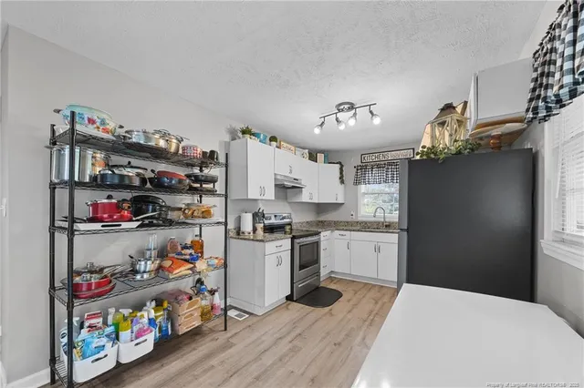 a kitchen with granite countertop a refrigerator a sink dishwasher a stove and white cabinets next to a window