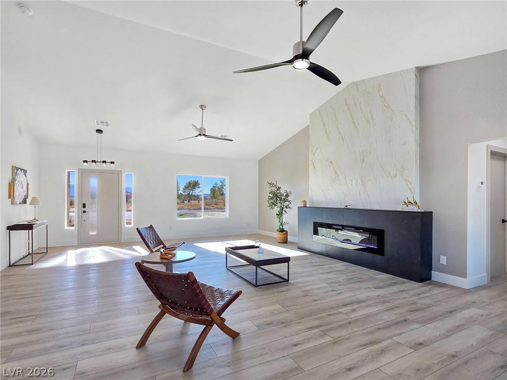 1120 West Gamebird Road Pahrump, NV 89048 - Photo 13 of 36 Living area featuring a tiled fireplace, light wood-style floors, ceiling fan, and high vaulted ceiling